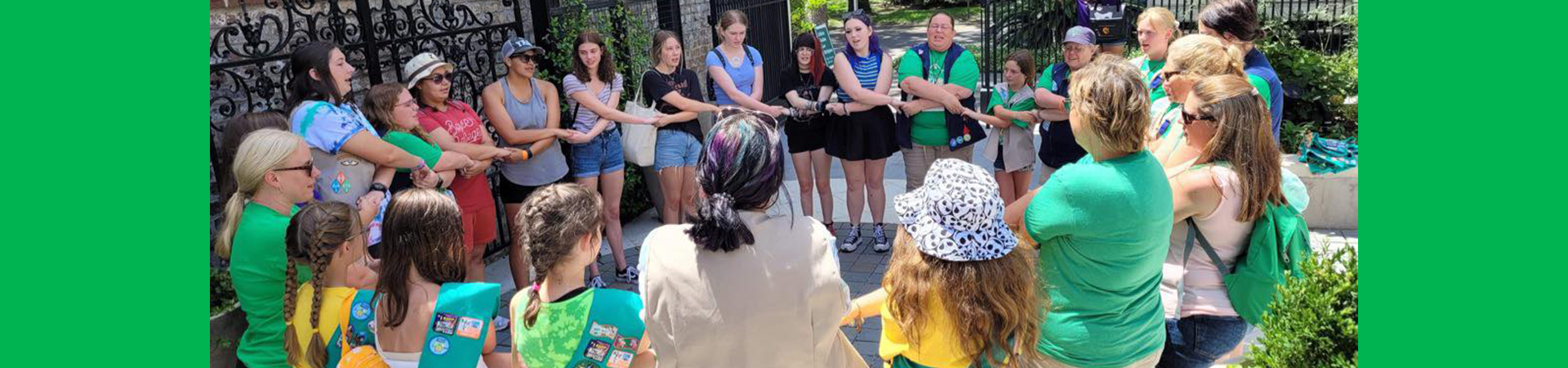  girl scouts and adult leaders hand in hand singing together in a circle outside 